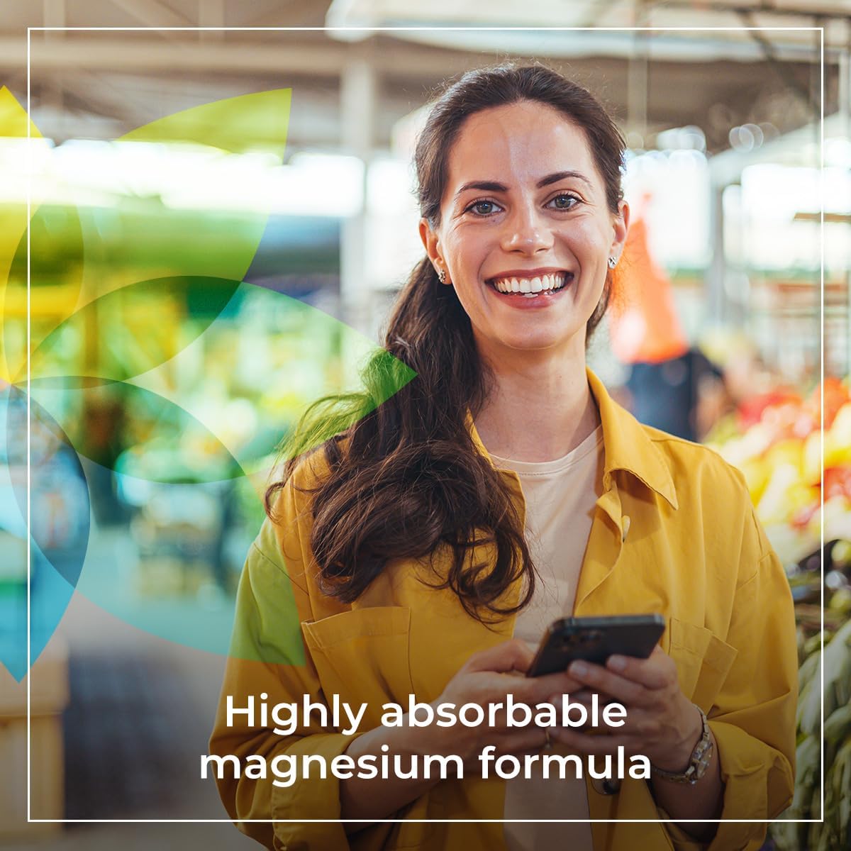 Woman in a yellow jacket holding a phone with text about magnesium formula, blurred indoor background